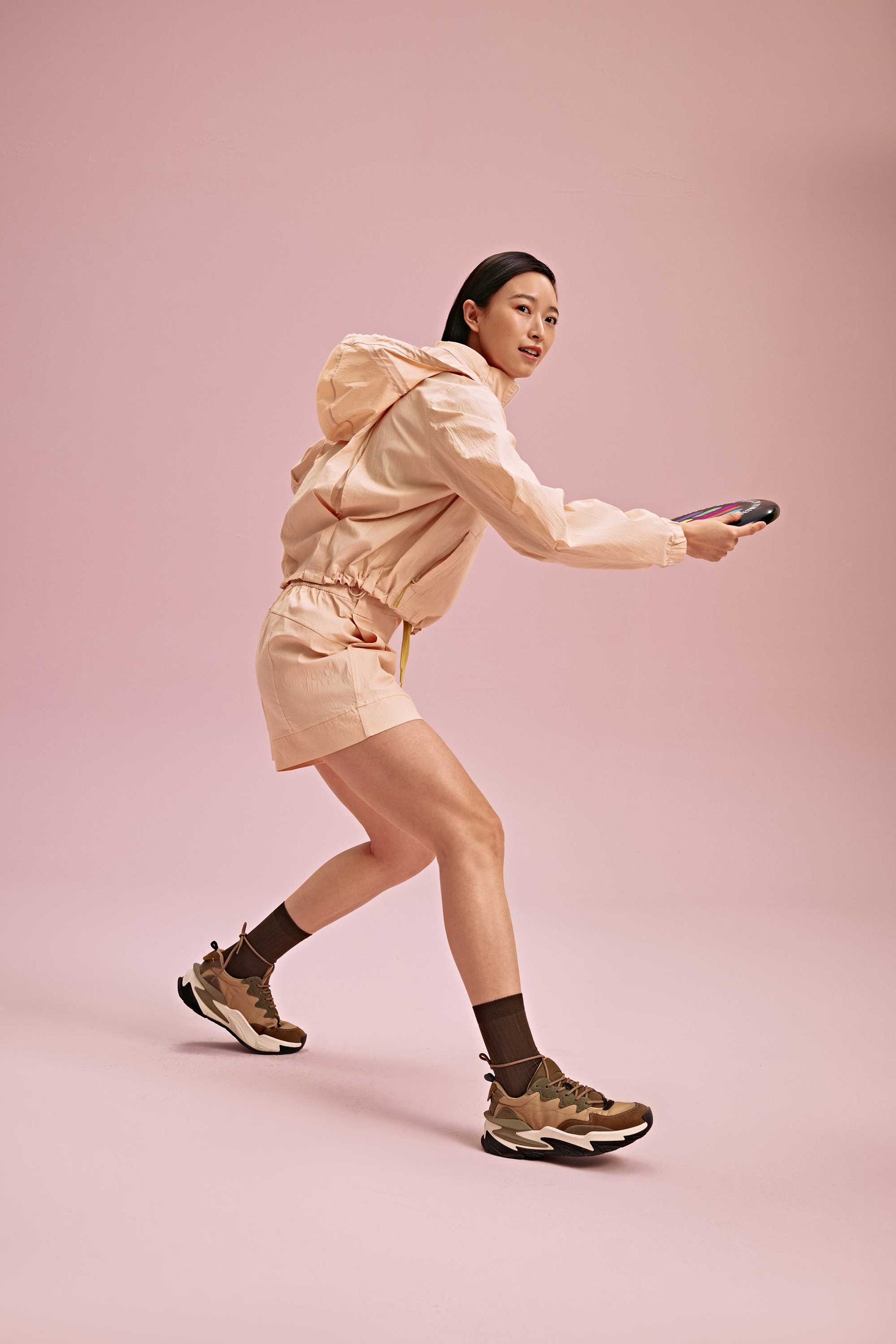 a woman wearing a warm yellow jacket and shorts play frisbee. she wears brown socks and shoes.