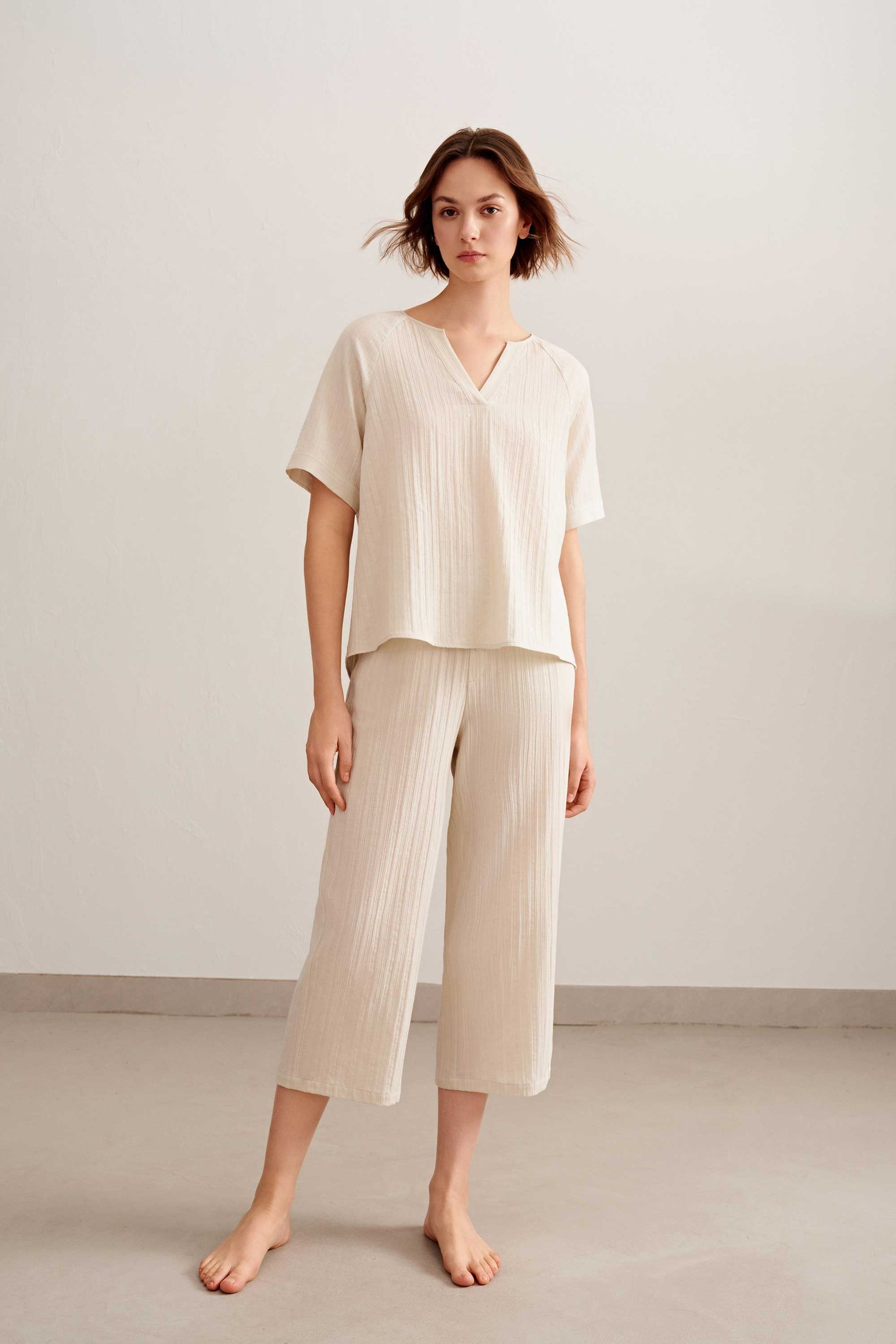 a woman wearing a light beige short sleeve v neckline tee and pants. 