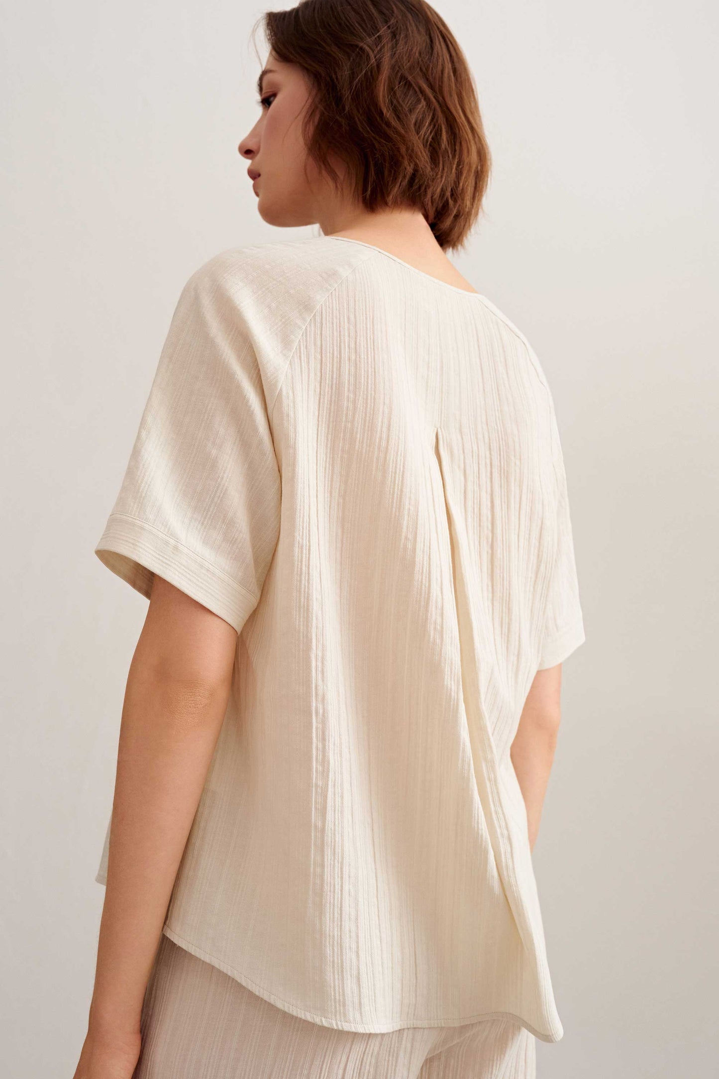back of a woman wearing a light beige short sleeve tee and pants. 