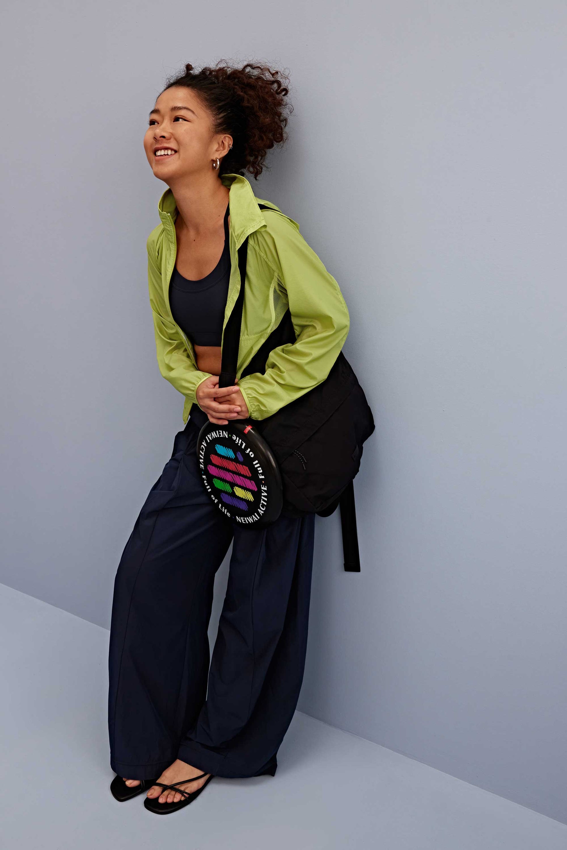 a woman wearing a green jacket and black sports bra, pair with navy pants and black bag