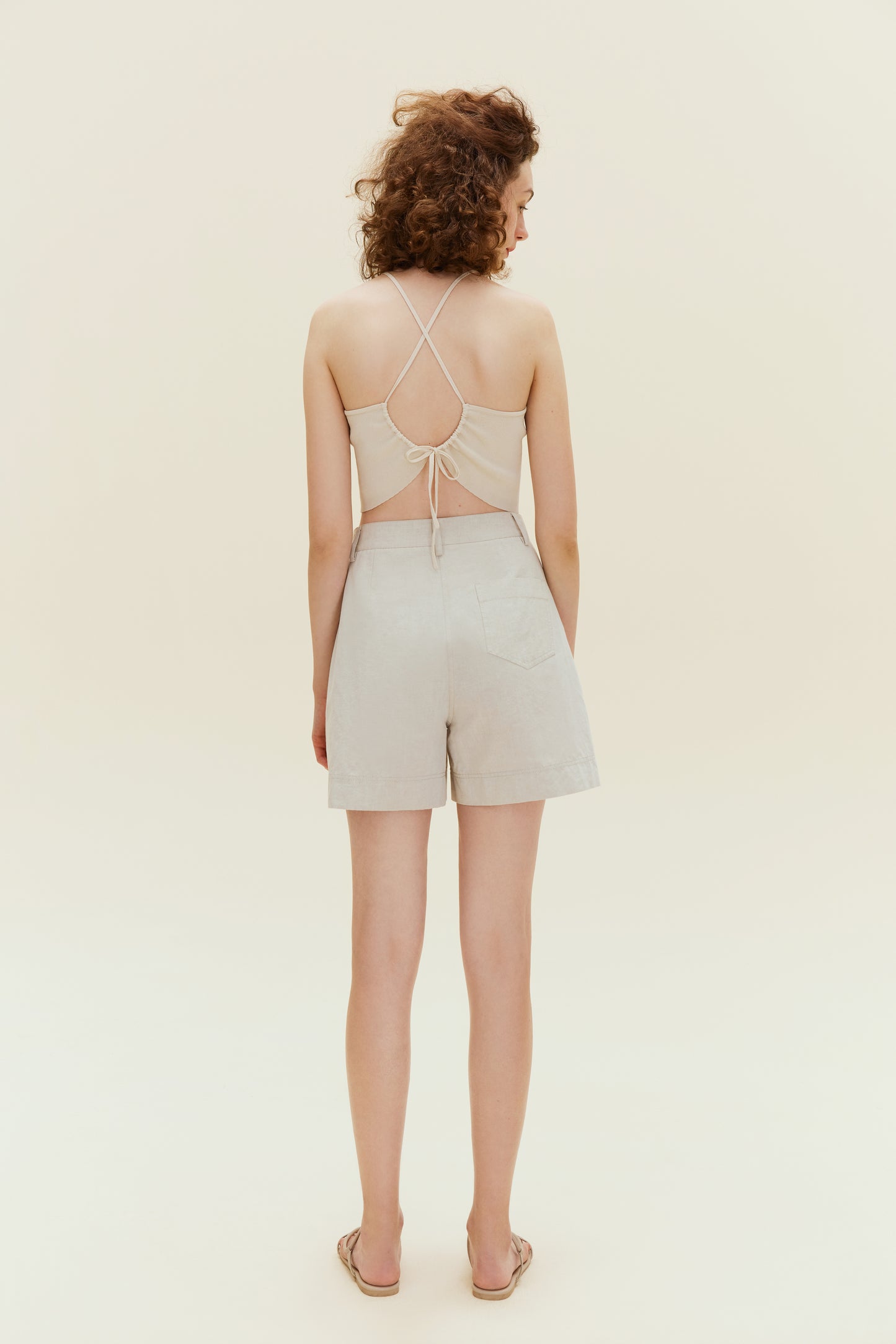 Back view of woman standing wearing beige tank top with khaki shorts