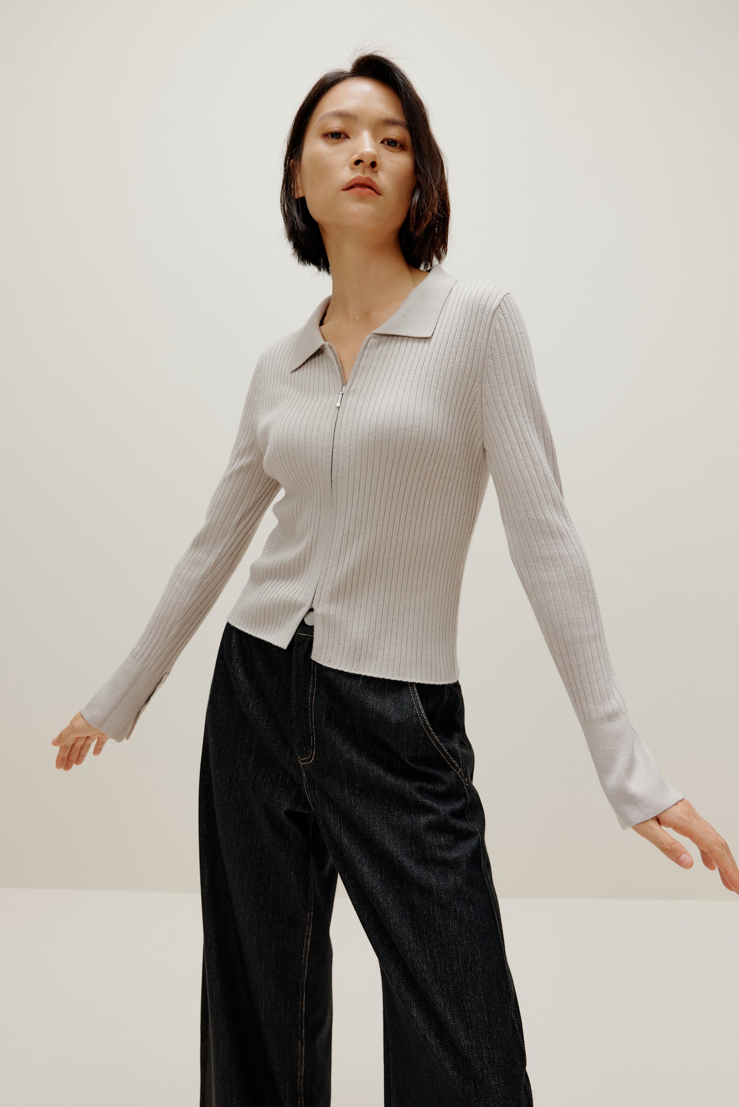 A woman wears a gray silky wool zip-up cardigan and black pants.