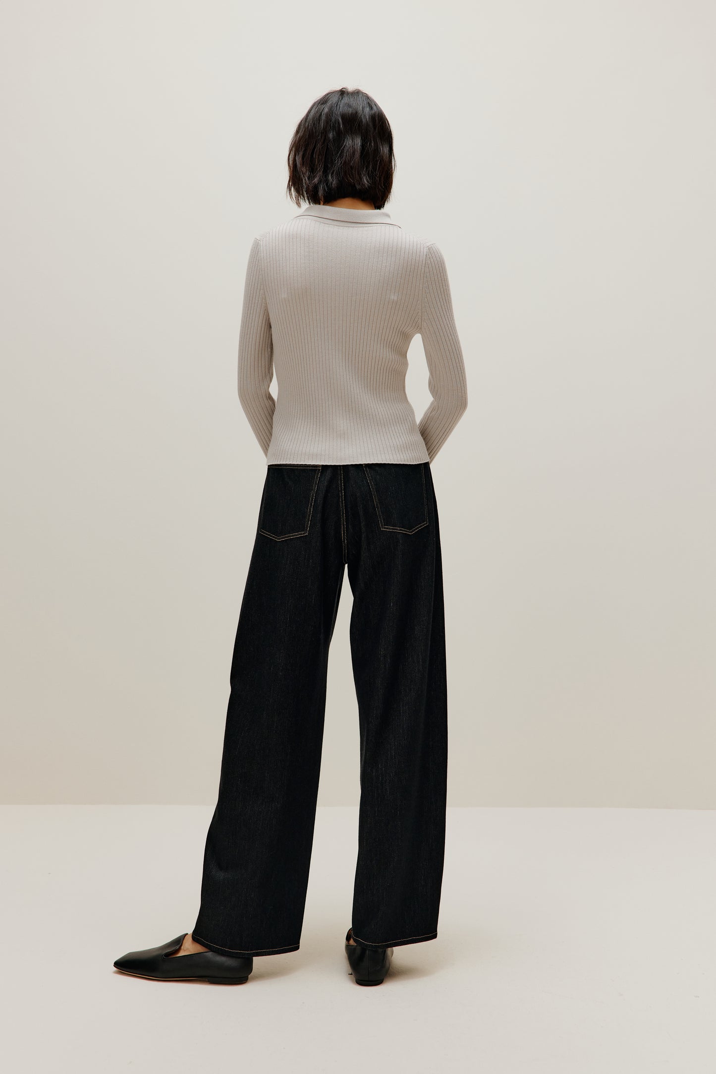 A woman wears a gray silky wool zip-up cardigan and black pants from back