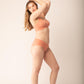 Side view of woman wearing spaghetti strap pullover bra in coral and matching underwear