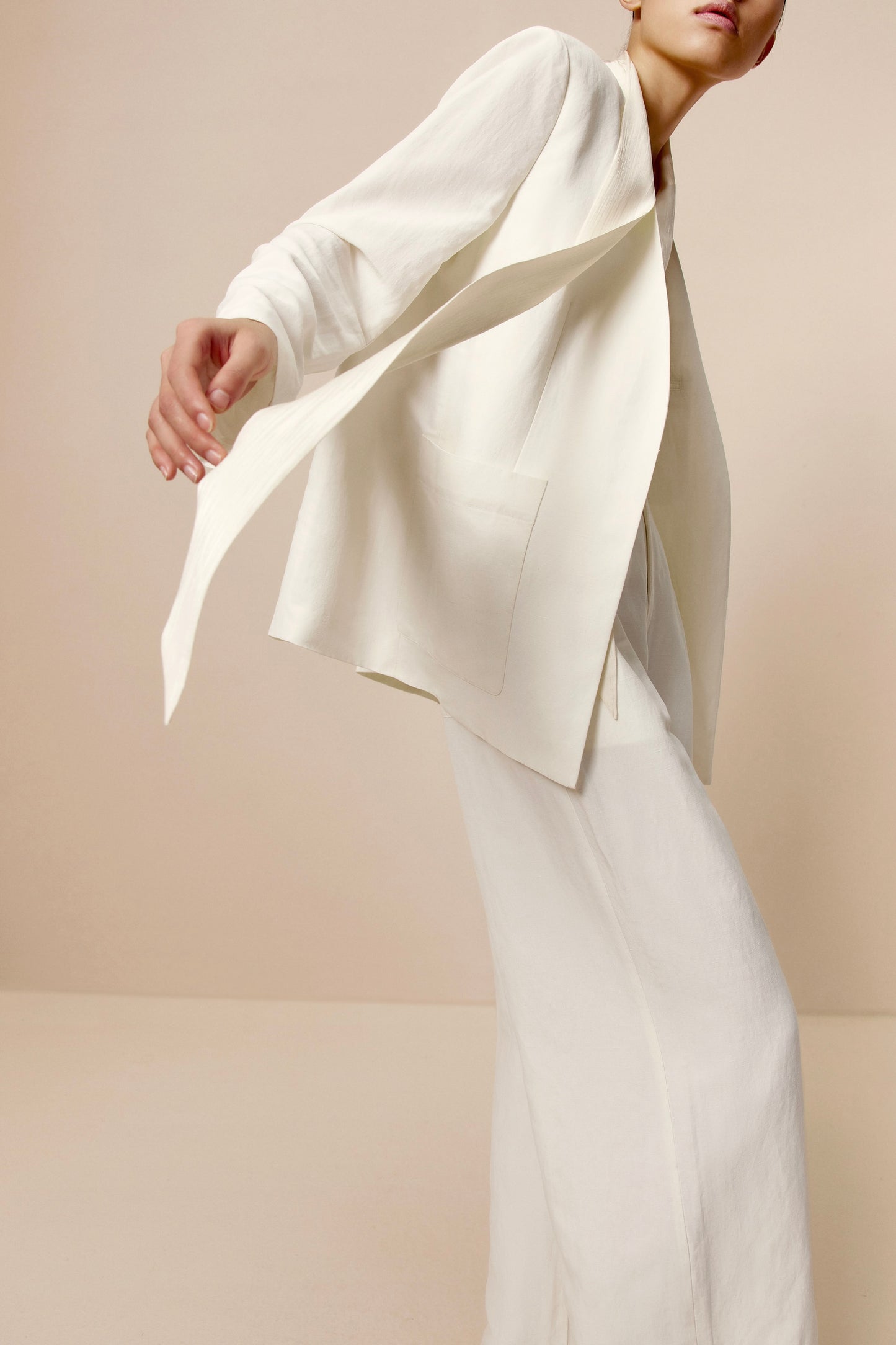 Side view of model wearing ivory blazer with matching ribbon tie and pants.