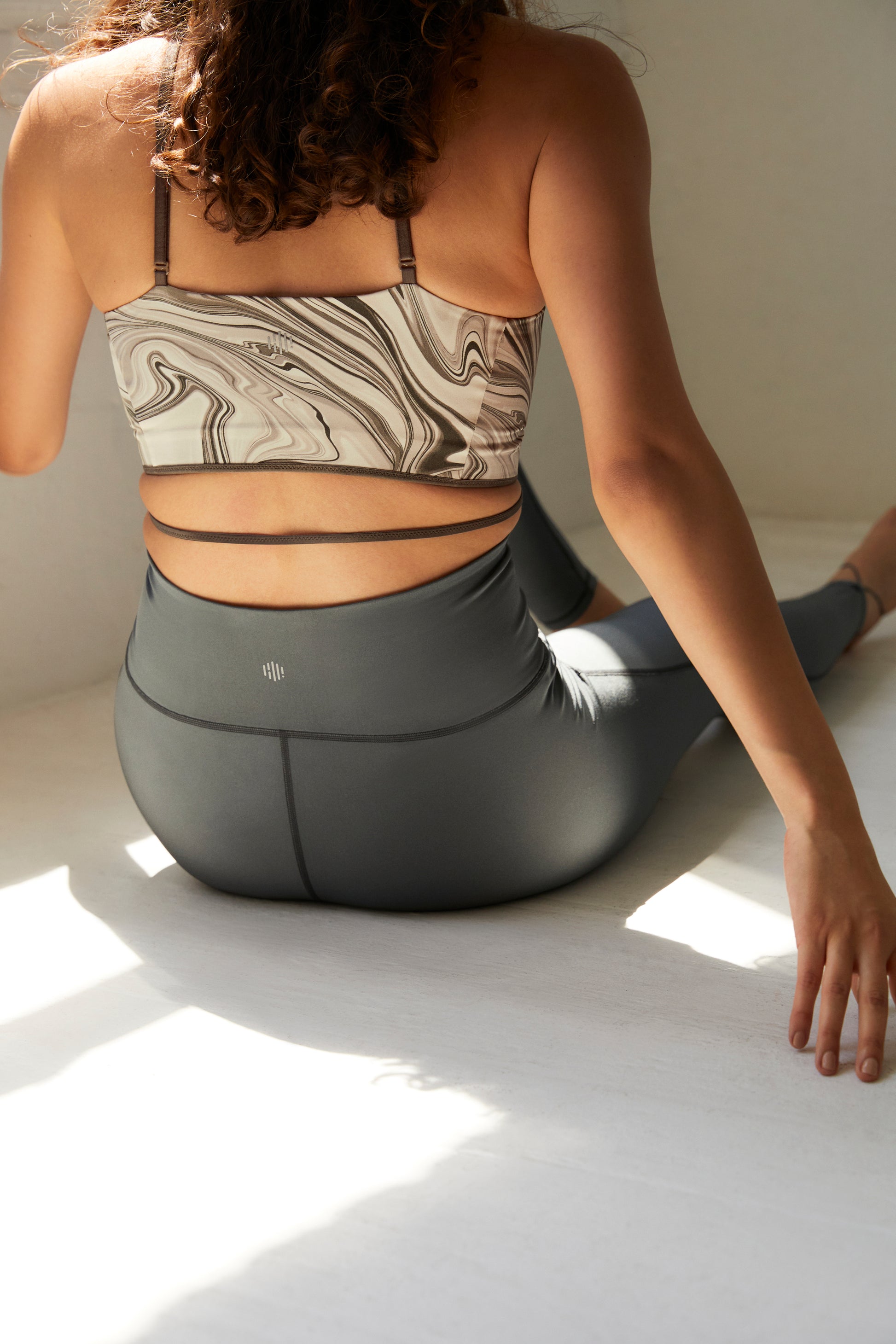 back of a woman wearing a marble print sports bra, dark grey leggings.