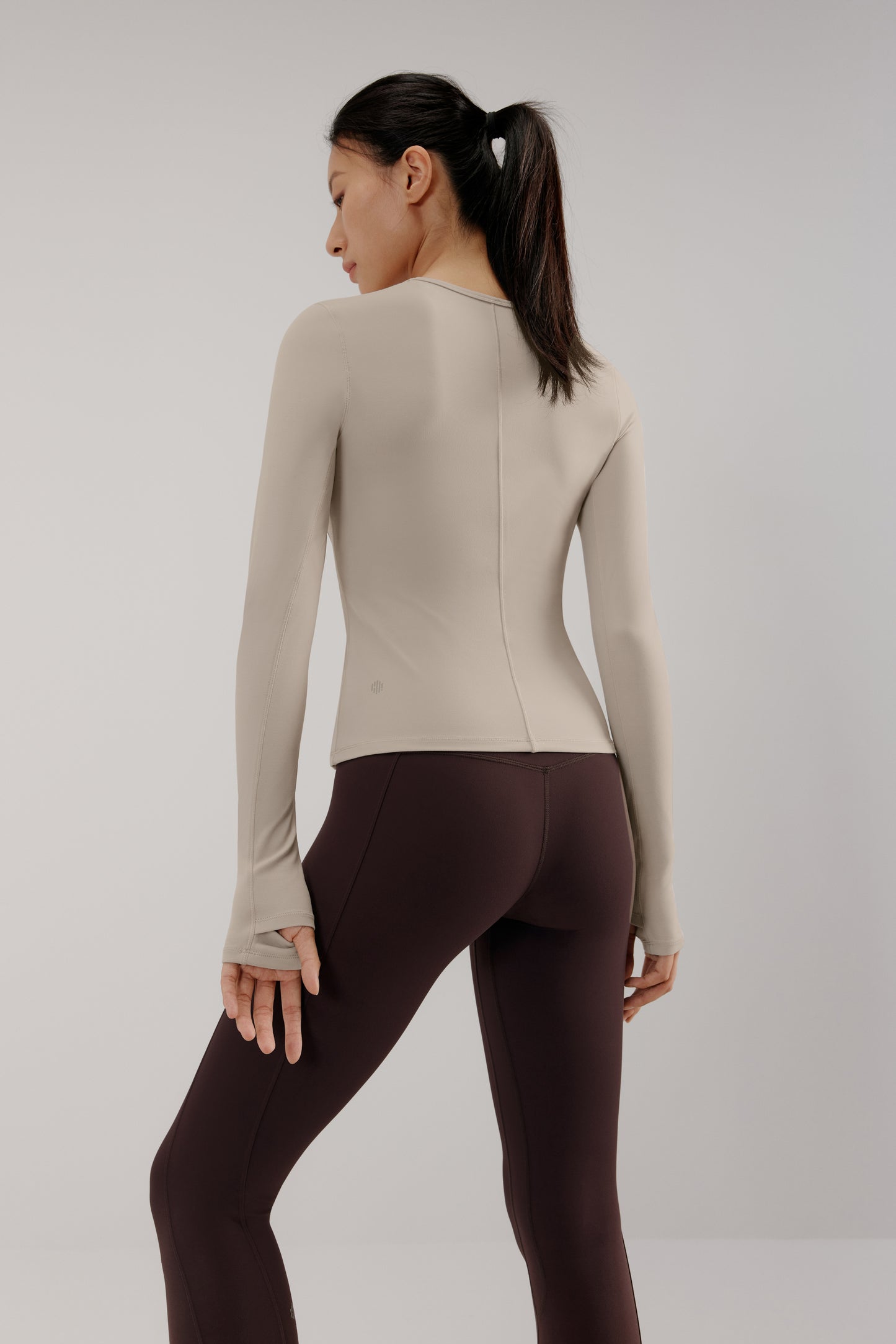 A woman wears a grey mousse long sleeve sports top and brown leggings from back