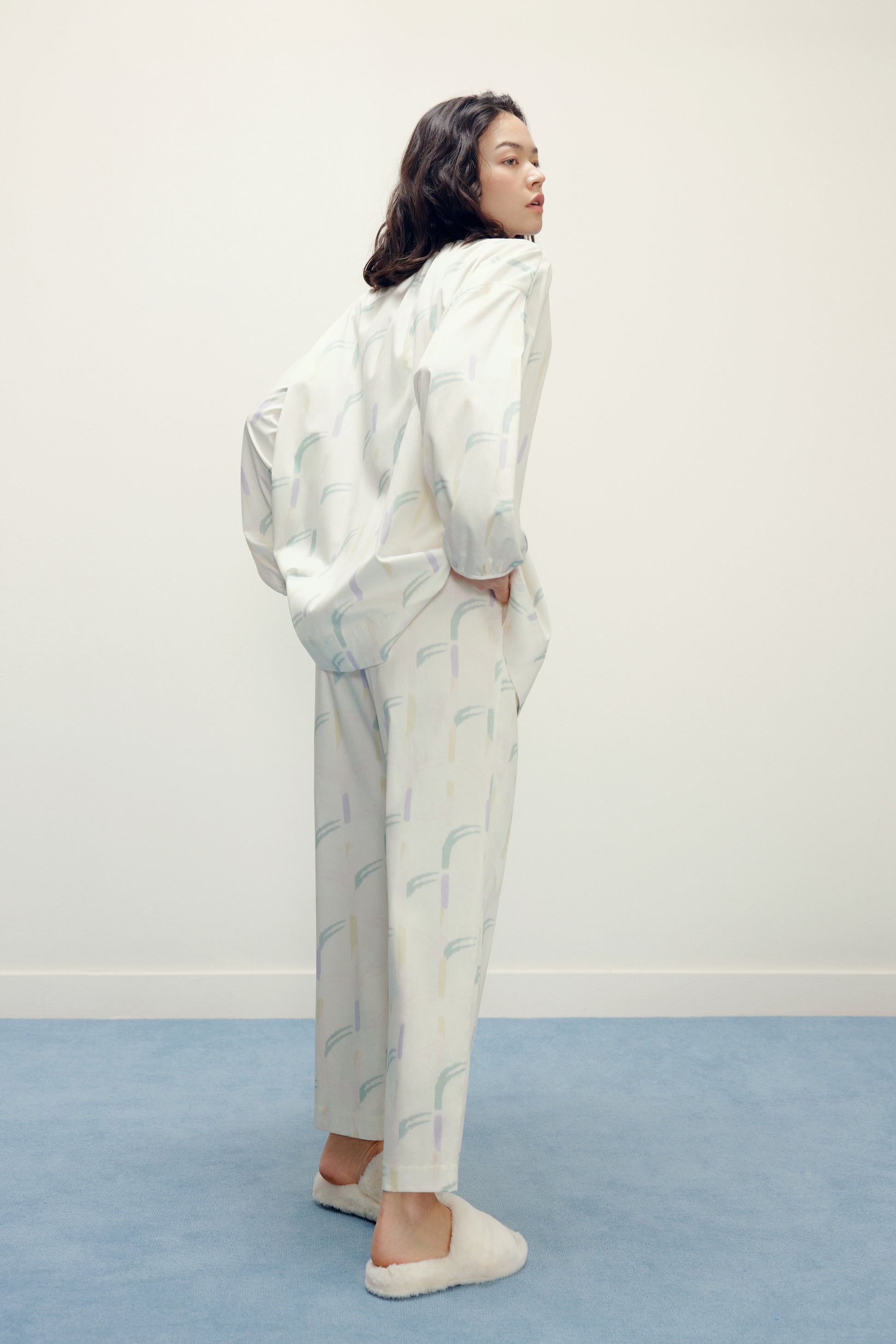 back of a woman wearing a white pajama sets with pattern and white slippers