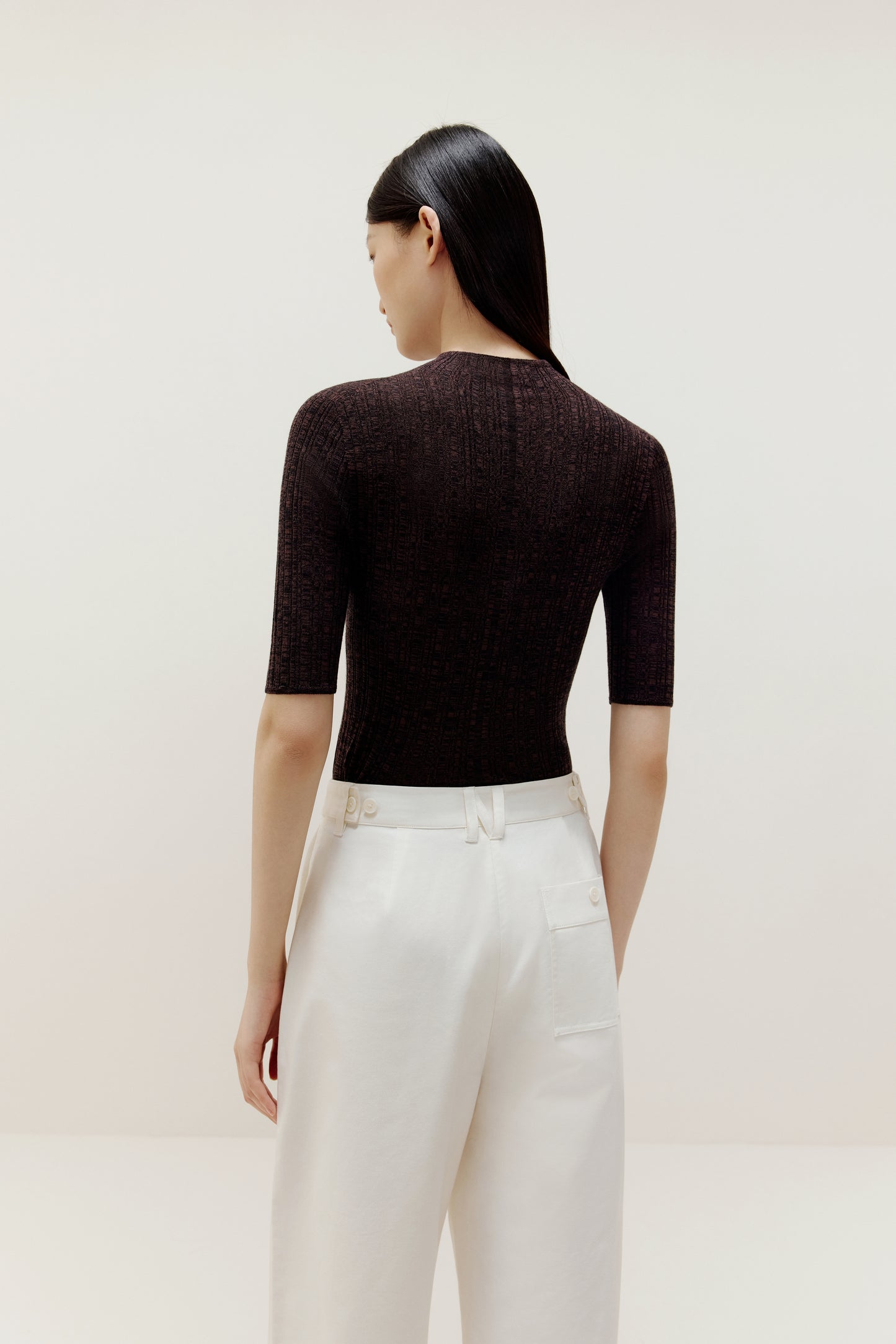 back of a woman wearing a brown sweater and white pants