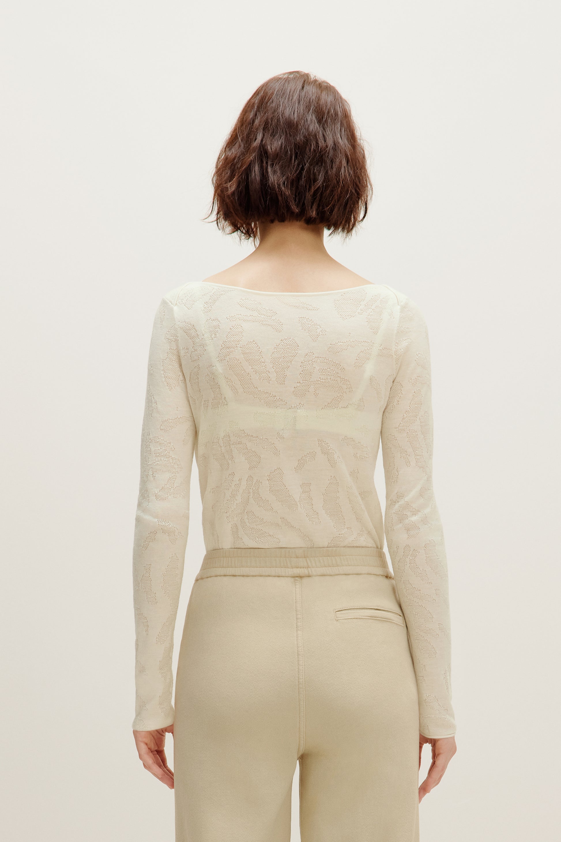 back of a woman wearing a white sweater and white pants