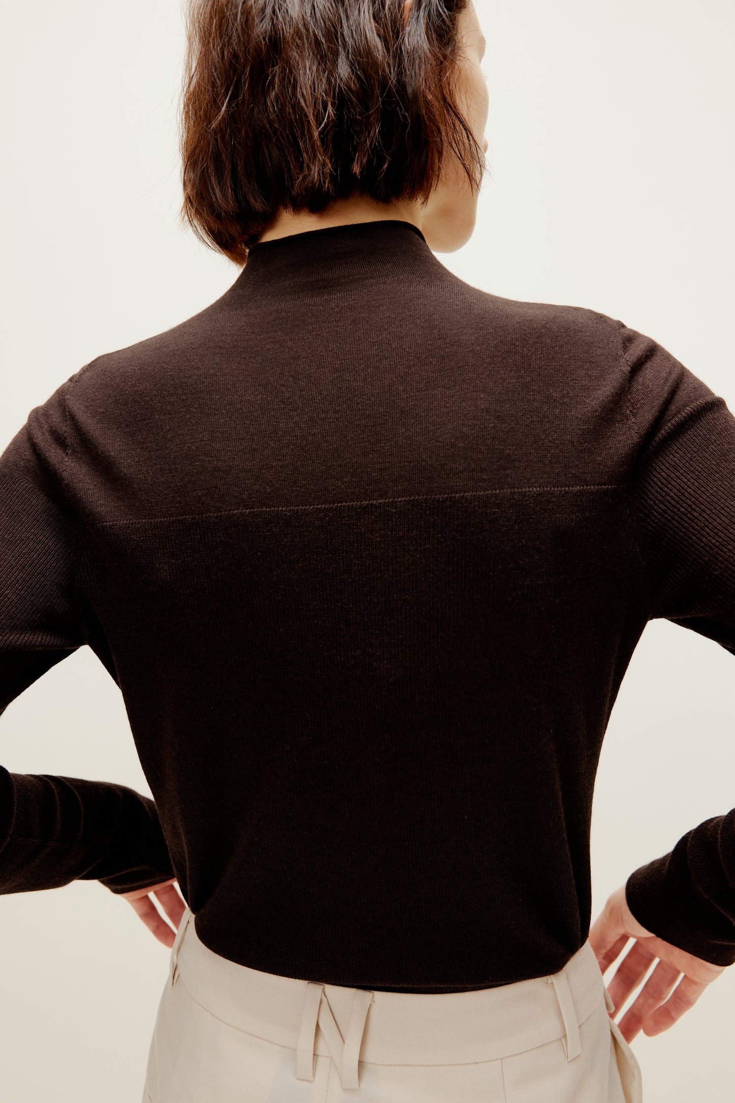 A woman wears a brown silky wool mock neck sweater from back