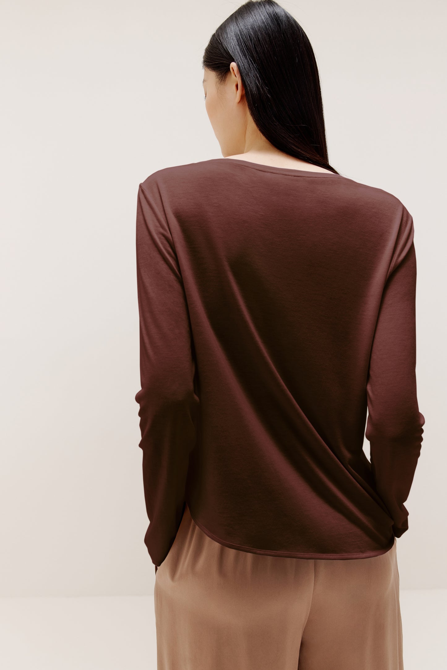 A woman wears a brown sweater and beige pants from back.