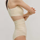side of woman in cream color cross over bra and high waist bottom