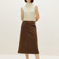 A woman wears a white silky wool mock neck sleeveless sweater and a brown skirt.
