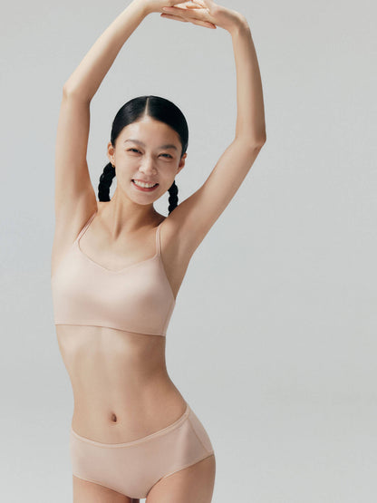 Model wearing nude bra and briefs with arms raised.