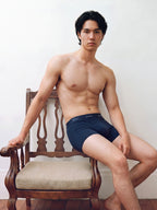 Male model in briefs seated on wooden armchair. Navy color.