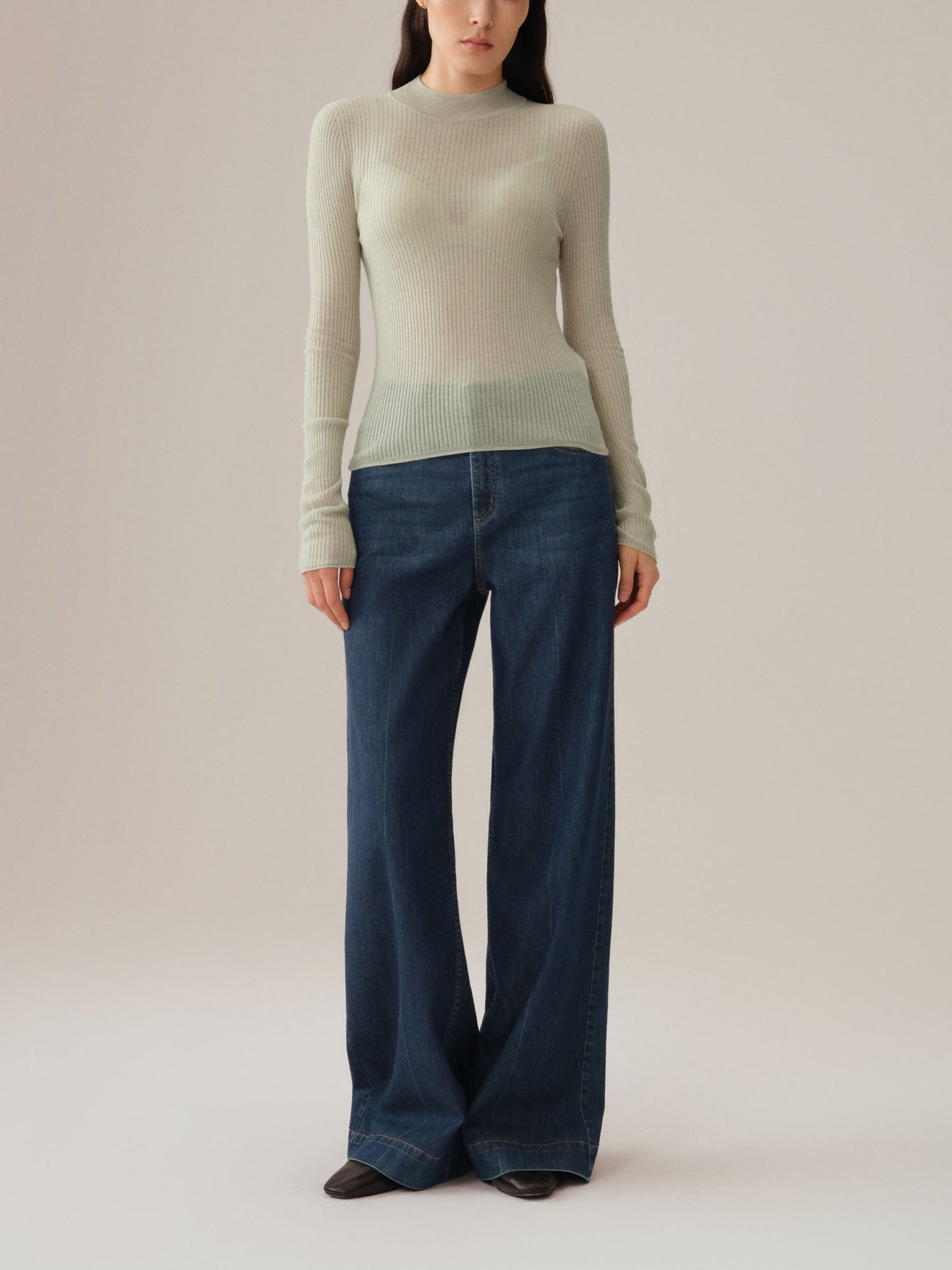 Model wearing a light green sweater and dark blue jeans on a plain background