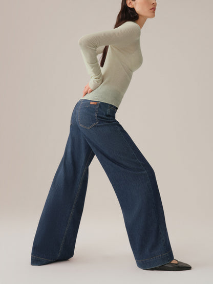 Model wearing a light green sweater and dark blue jeans on a plain background