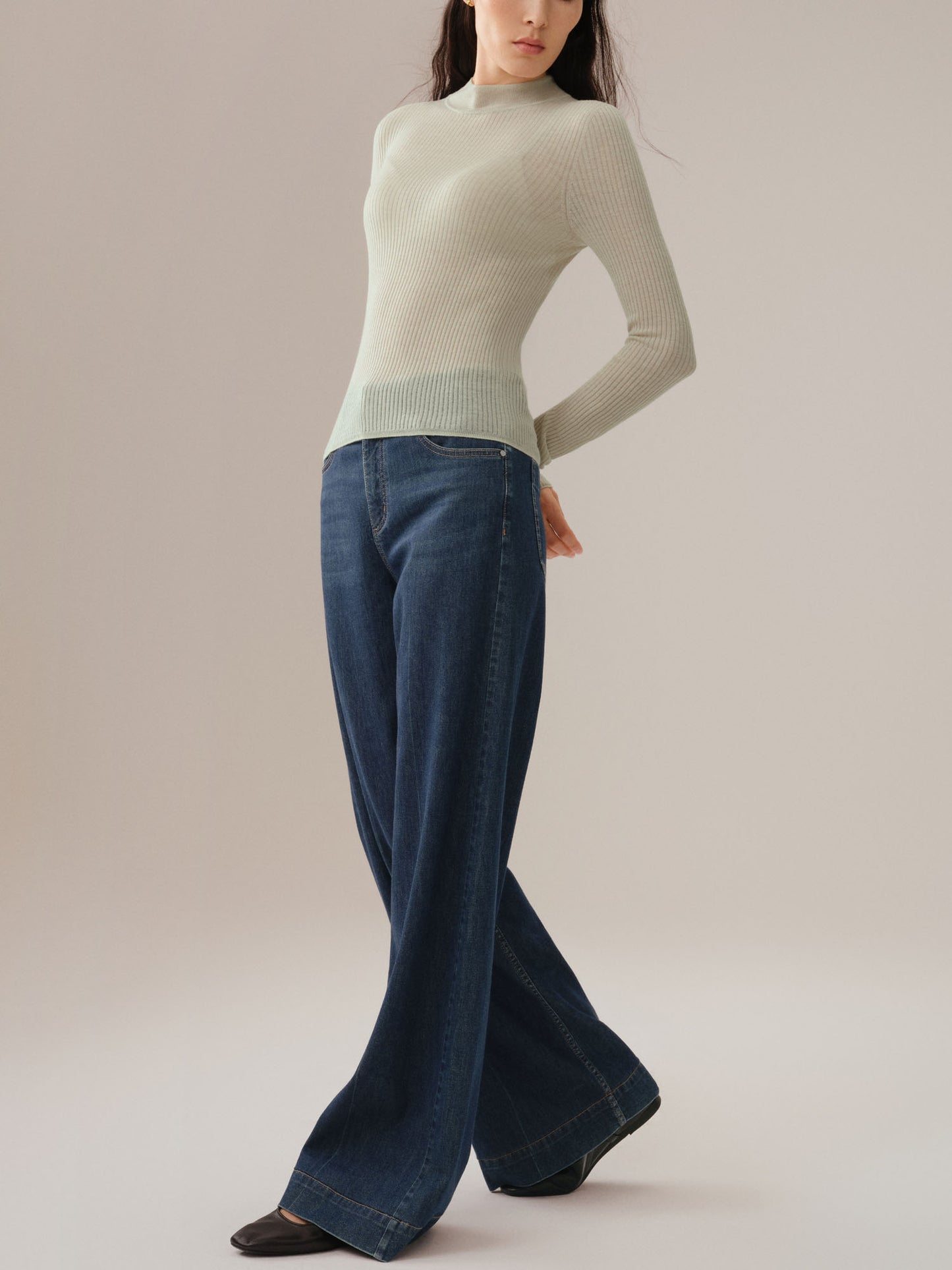 Model wearing a light green sweater and blue jeans on a plain background