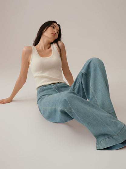 Model wearing a white tank top and blue jeans sitting on a light gray background