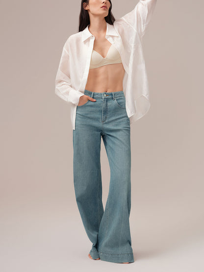 Model wearing a white blouse, beige bralette, and blue jeans on a plain background