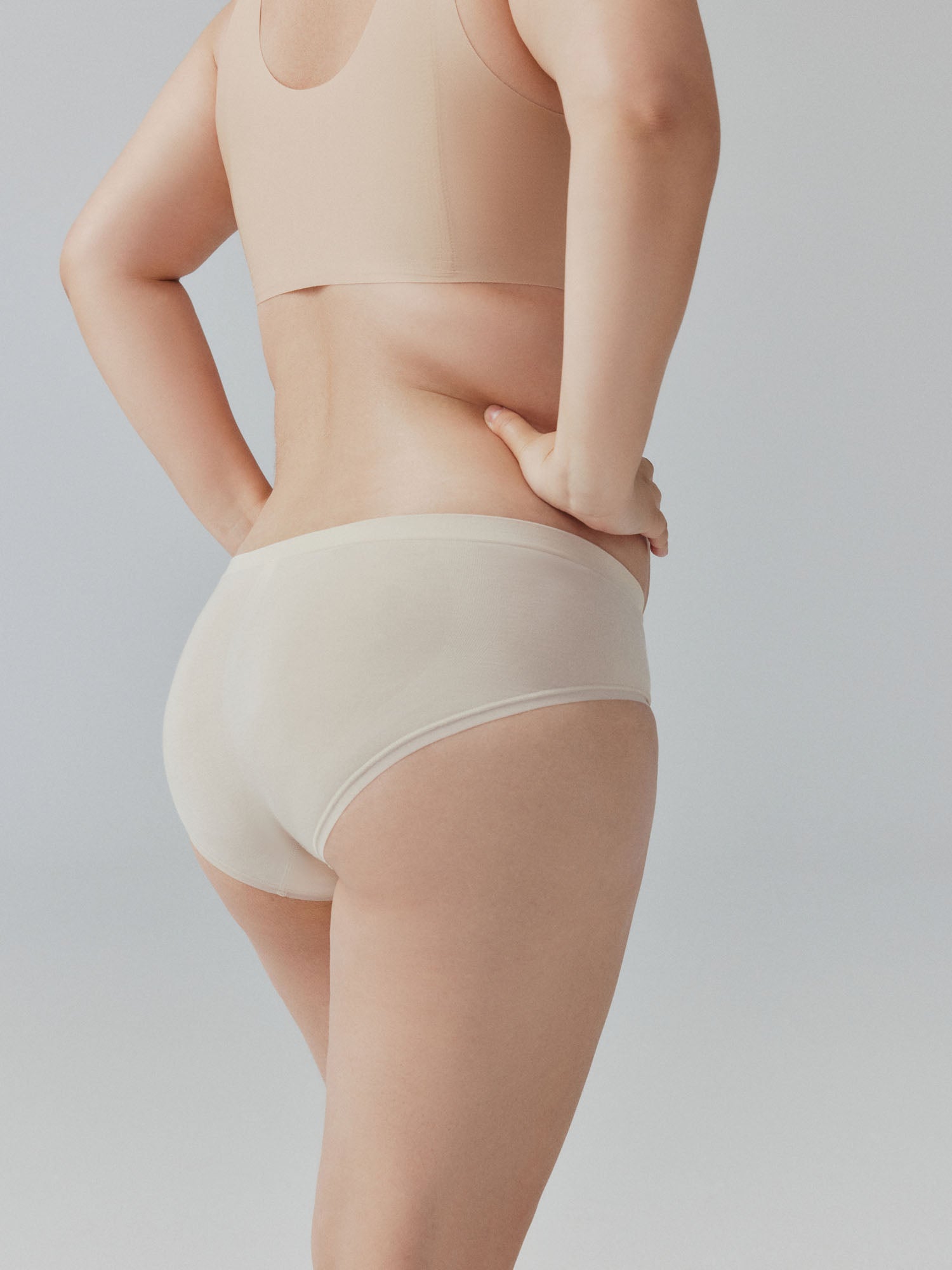 Model wearing beige tank top and underwear on a plain background.