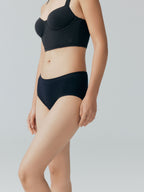 Model wearing a black bra and brief set on a plain background.