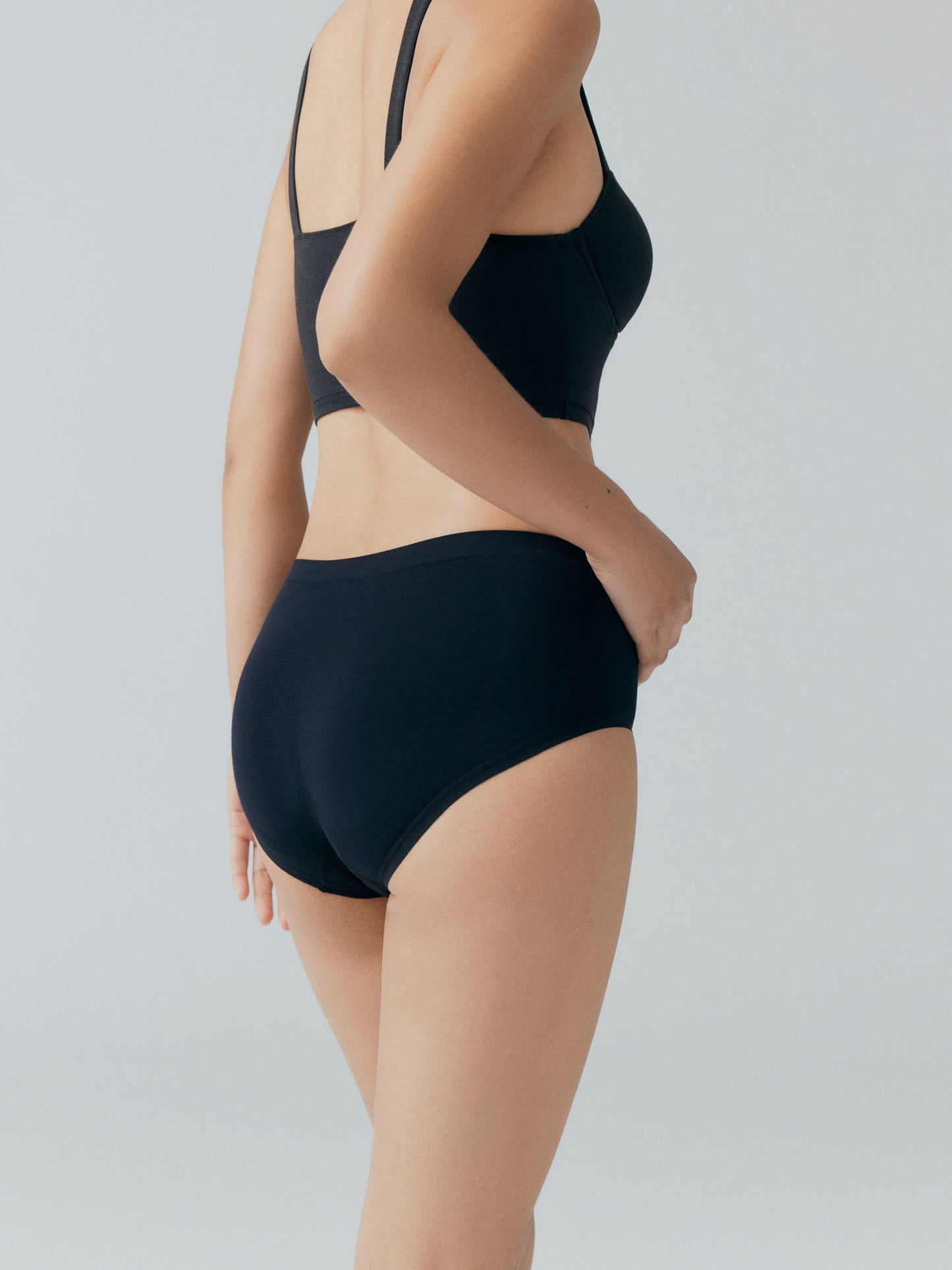 Model wearing a black bra and brief set on a plain background.