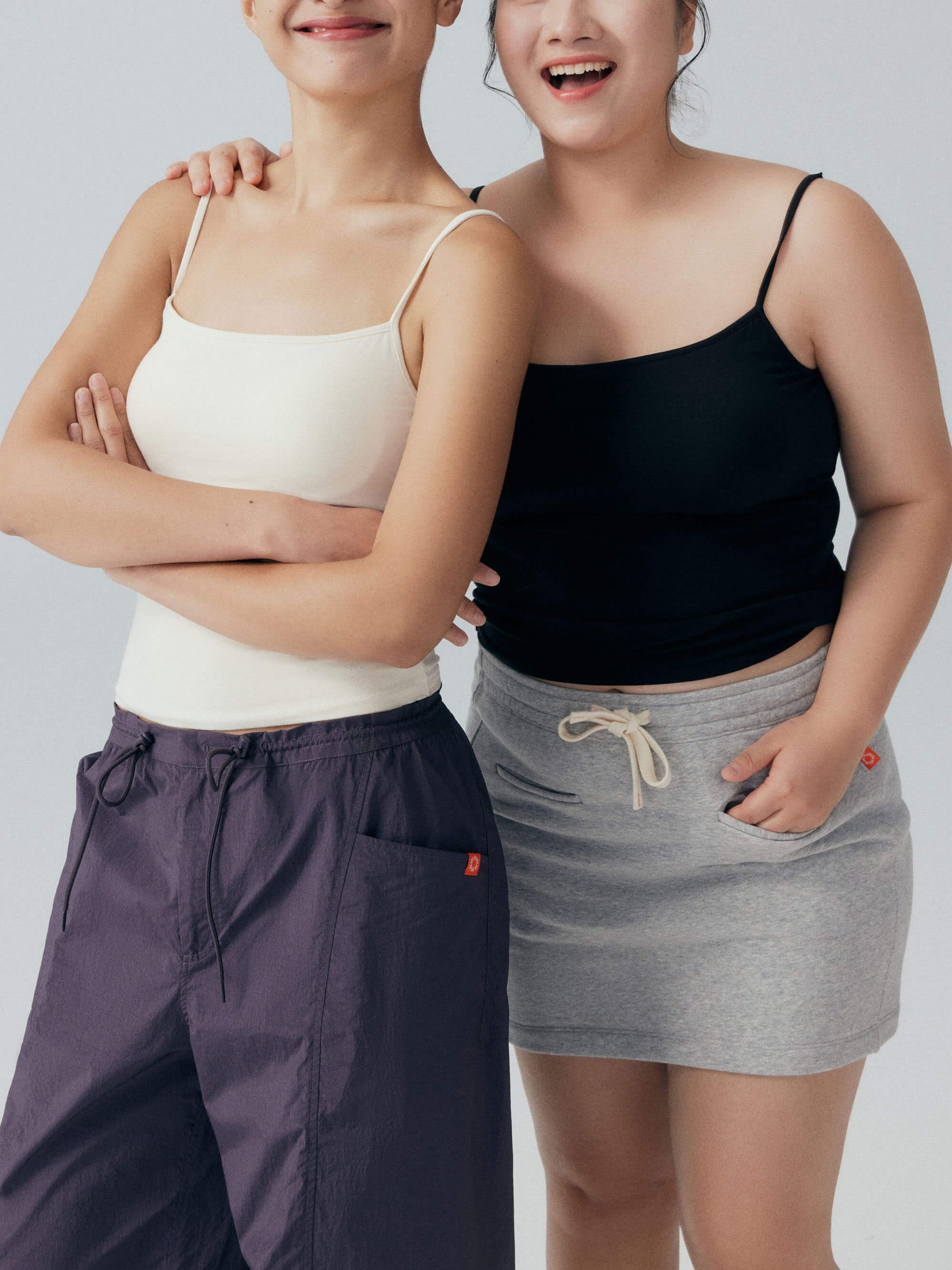 Two models smiling and wearing black and white camisoles 