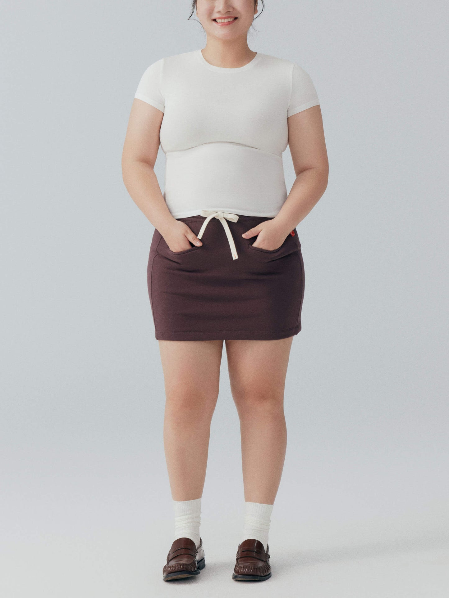 Model wearing white tee and brown skirt.