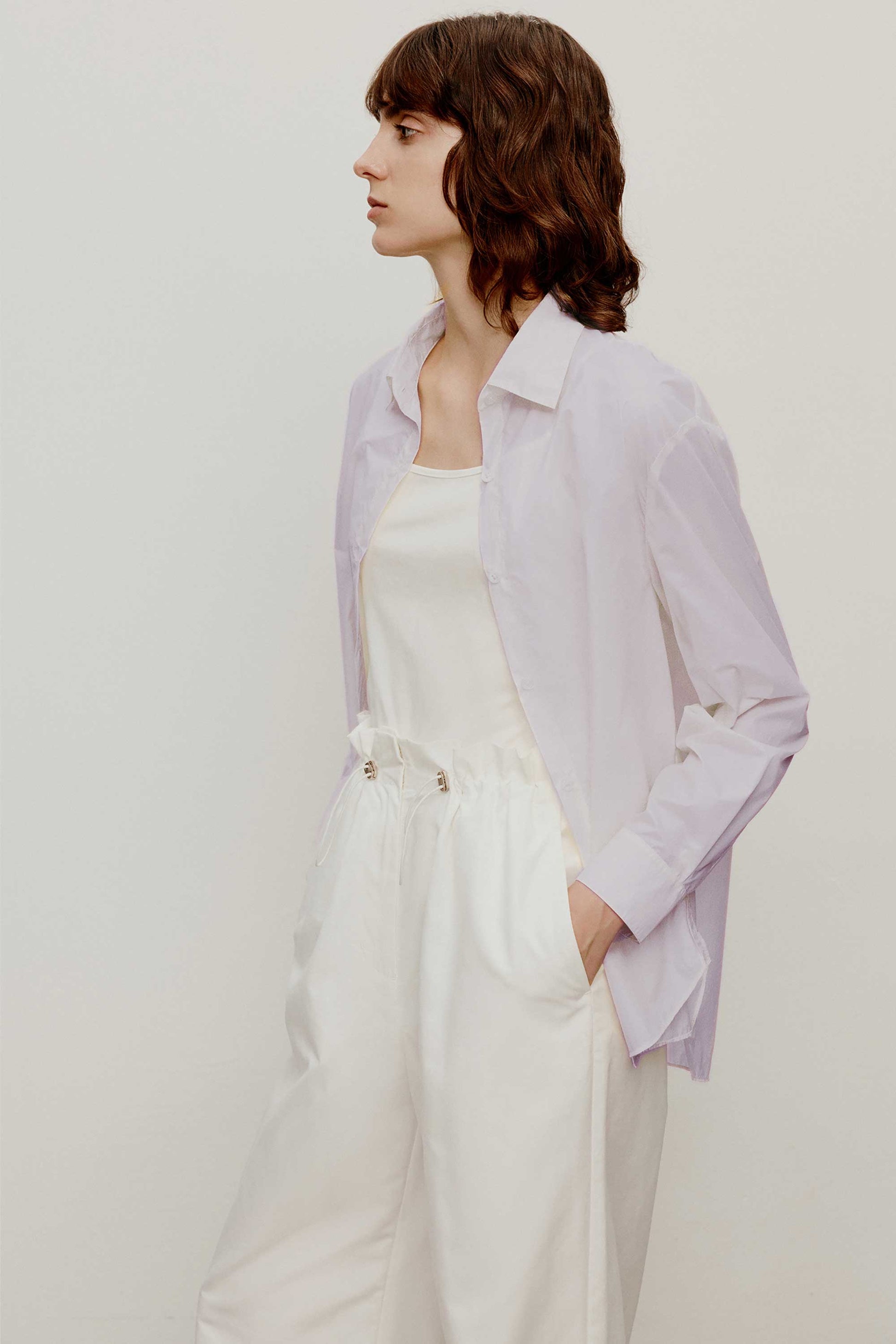 side of a woman wearing a light purple shirt with white camisole underneath and a white pants.