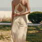 Back view of woman standing on grass wearing cream colored dress with thin straps and cross back design