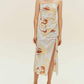 Woman standing wearing spaghetti strap dress with brown, beige, white print with high slit on side