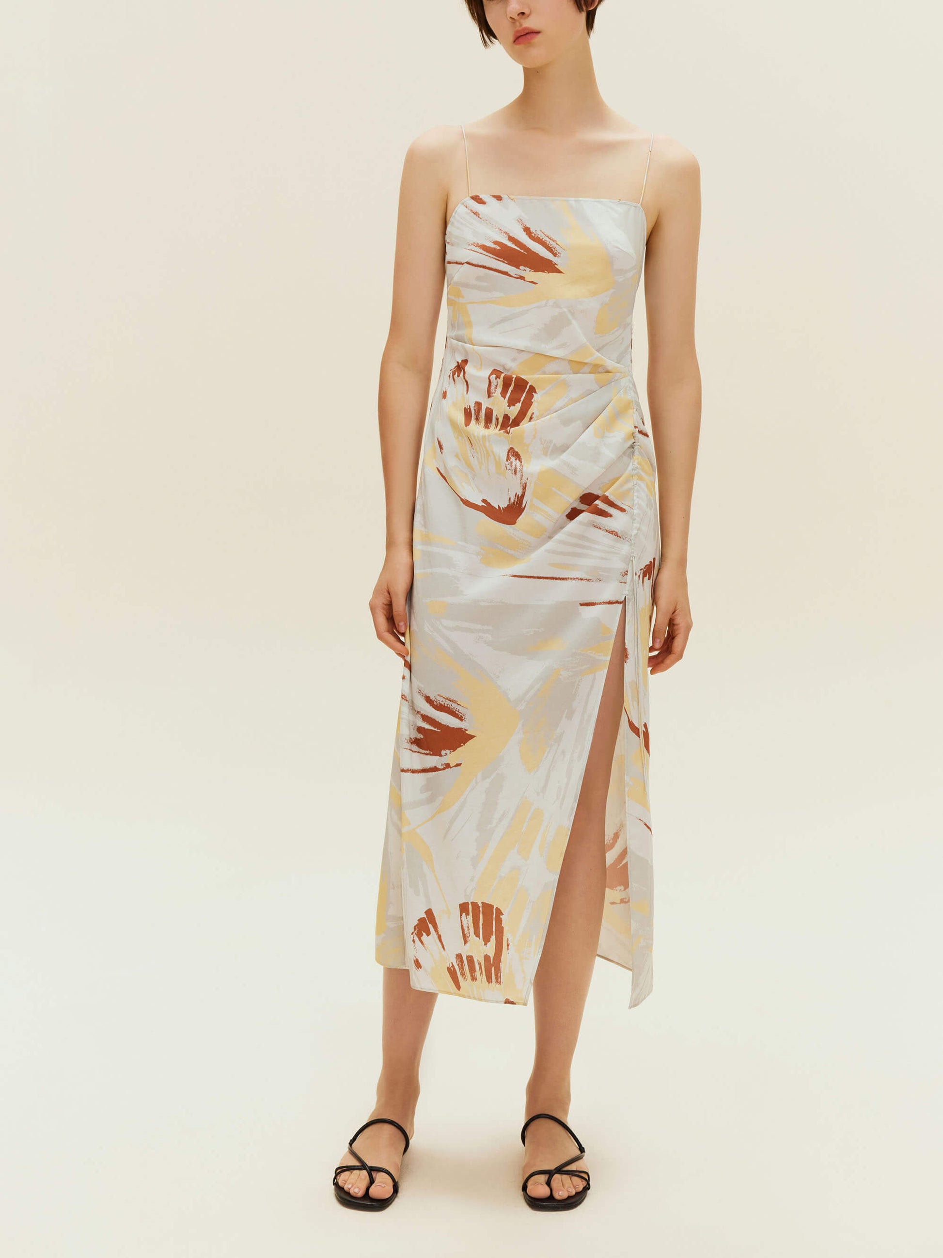 Woman standing wearing spaghetti strap dress with brown, beige, white print with high slit on side