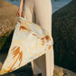 Woman standing on rock wearing off white knit pants holding printed scarf blowing in the wind