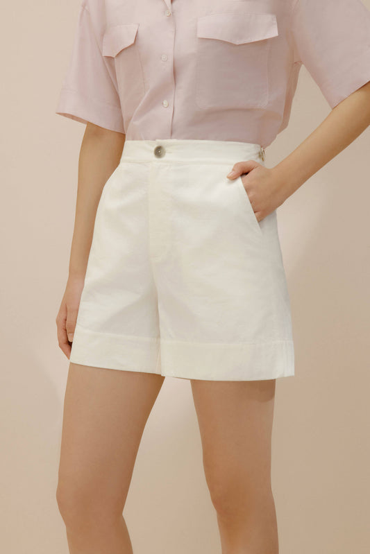 Model wearing light purple shirt and putting her hand into the pocket of white shorts. 