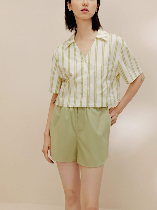 Woman wearing white and green short sleeved button up shirt and green pajama shorts