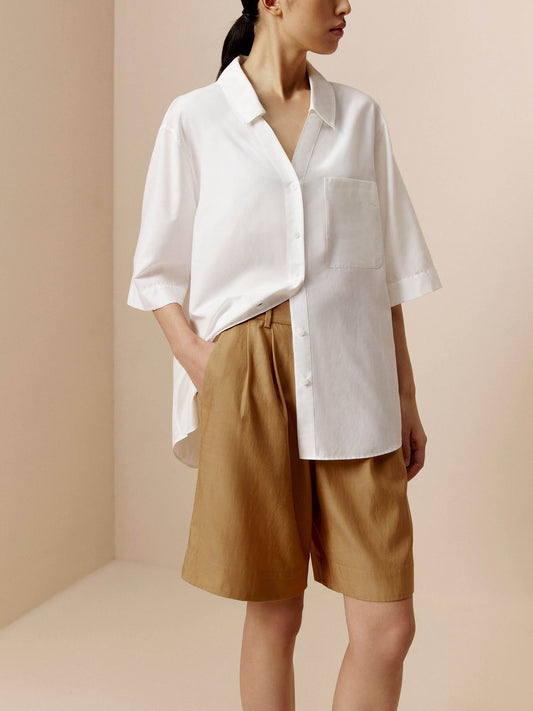 Woman wearing white short sleeve button down shirt and tan Bermuda shorts