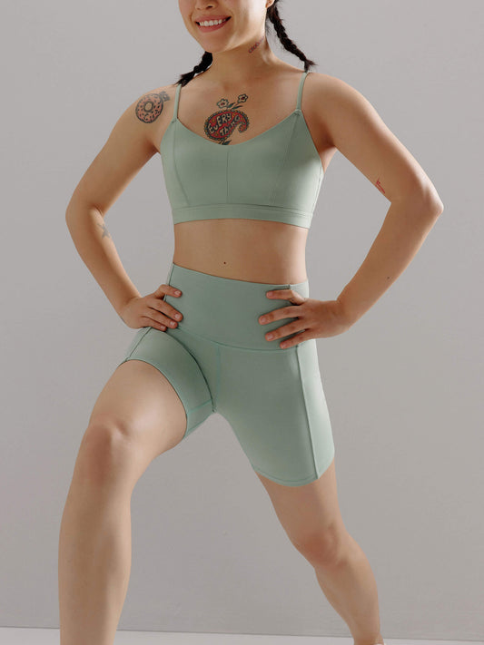 A woman wears a teal sports bra and shorts.