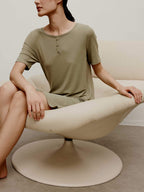 A woman in a green pajama dress sits on a white round sofa.