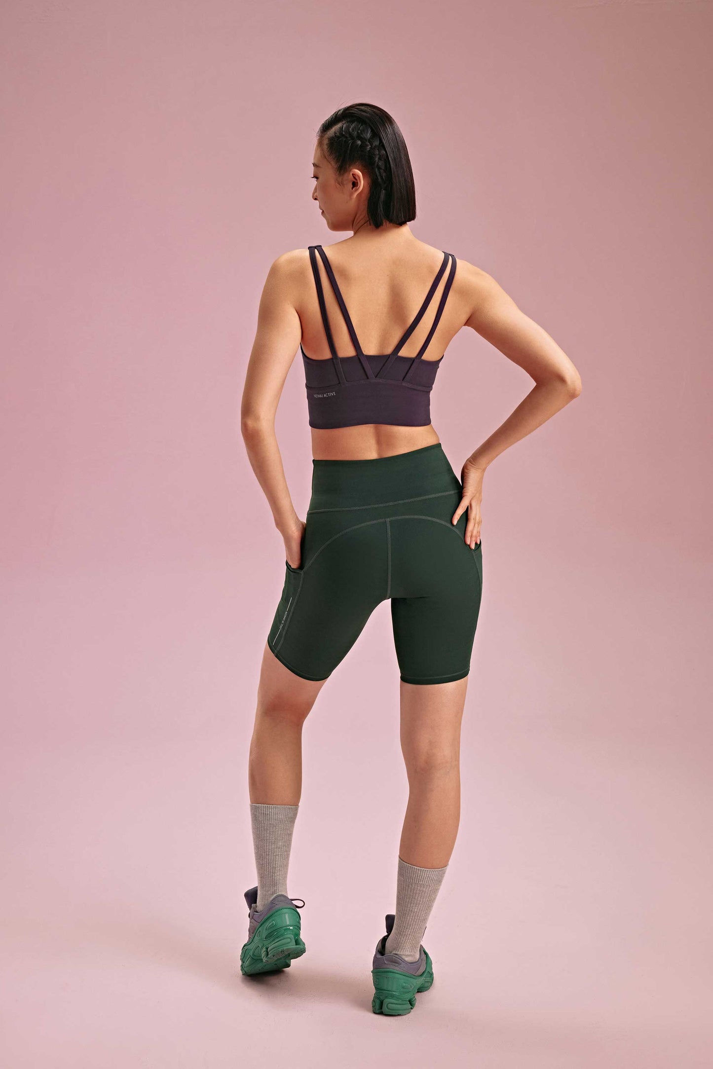 back of a woman wearing a black sports bra and green biker shorts. pair with grey socks and green shoes.
