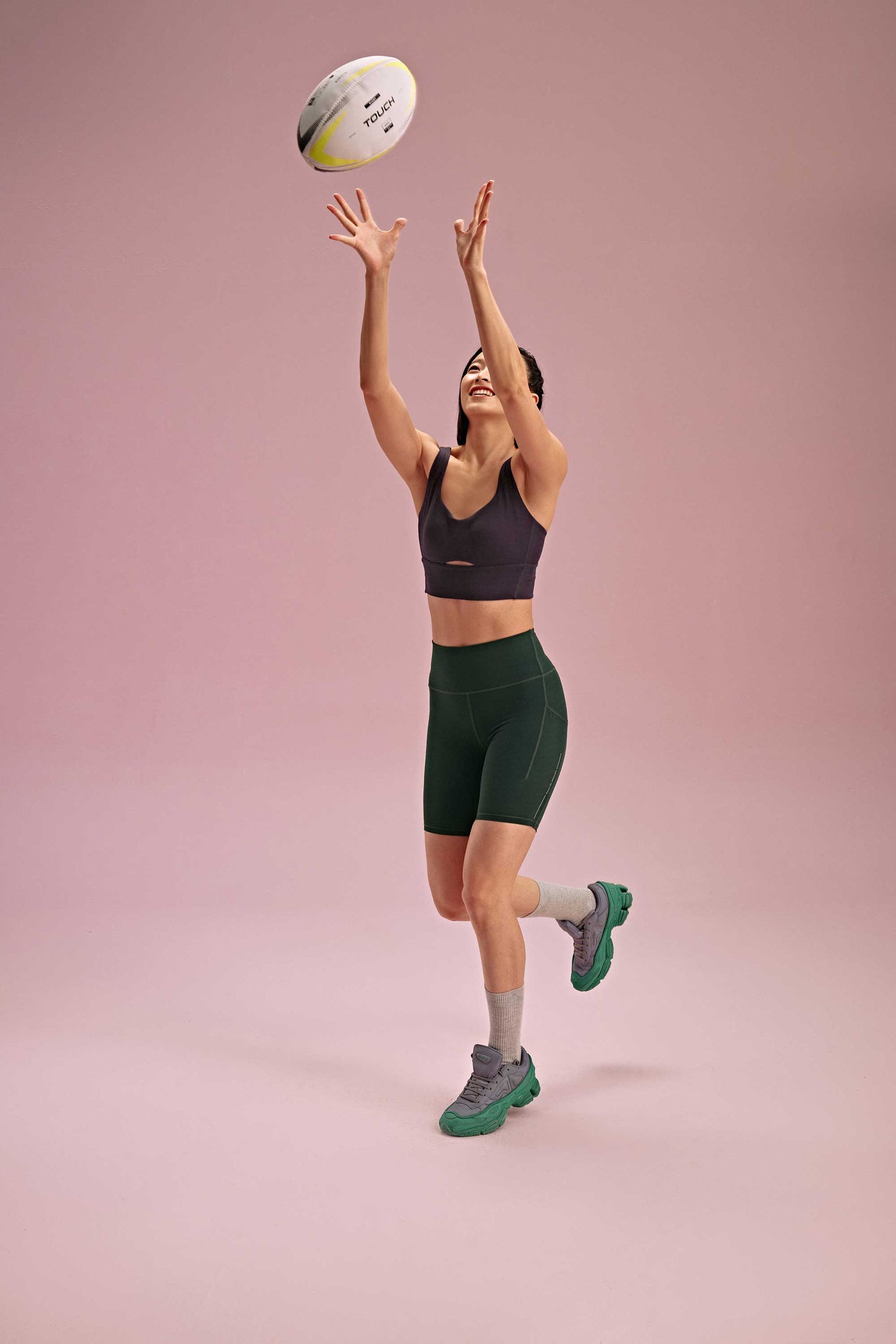 a woman throwing the ball wearing a black long sports bra and green biker shorts. pair with grey socks and green shoes.