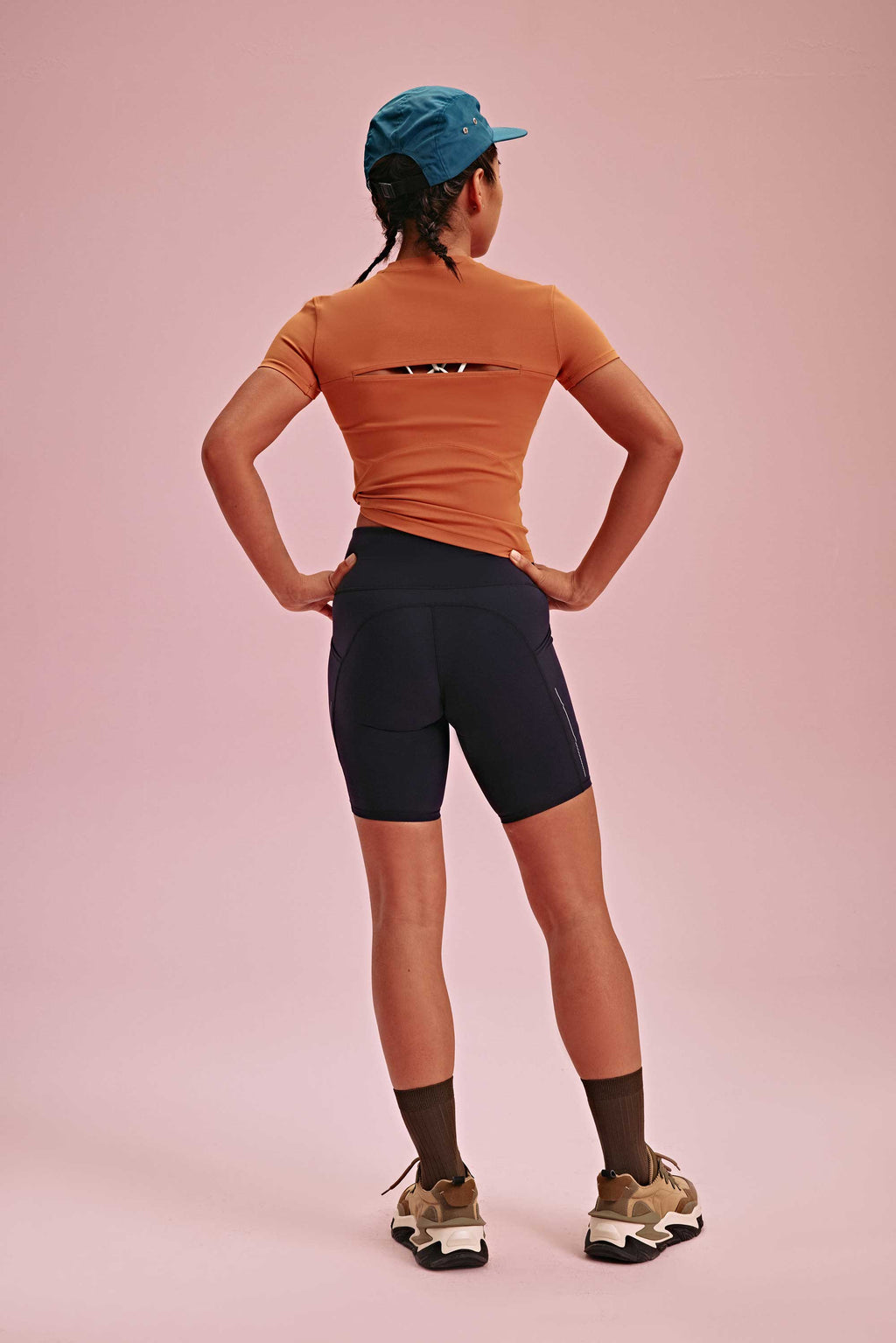back of a woman wearing blue hats, brown tee and black biker shorts. pair with brown socks and shoes.