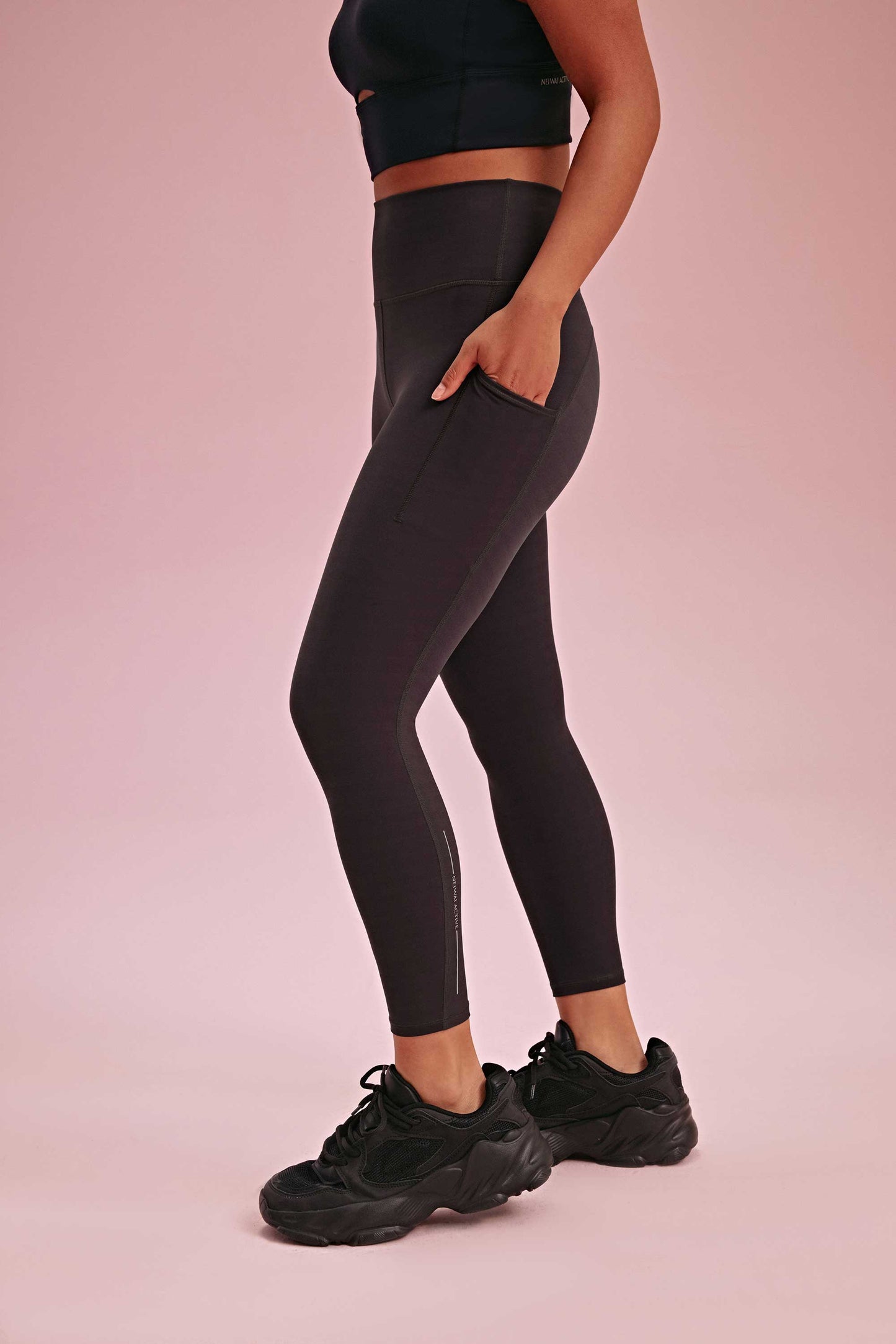 side of a woman wearing a black sports bra and black leggings with hands in the side pockets. she also wearing a black sneaker
