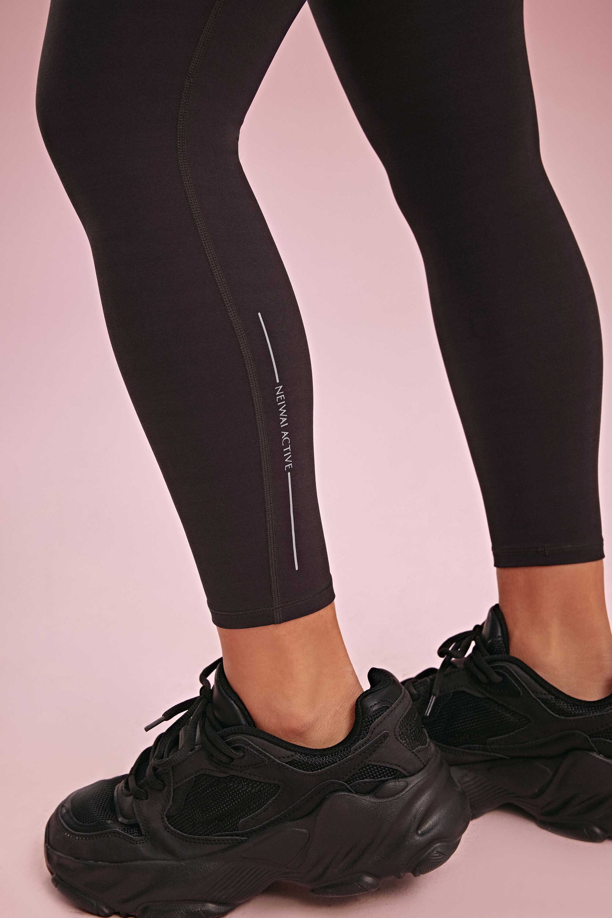 ankle detail of the black leggings shown neiwai active logo, she wears a black sneaker