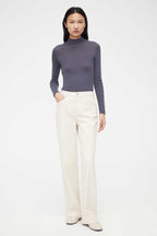 woman in purple mock neck sweater and white pants