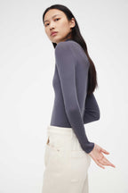 side look of woman in purple mock neck sweater and white pants
