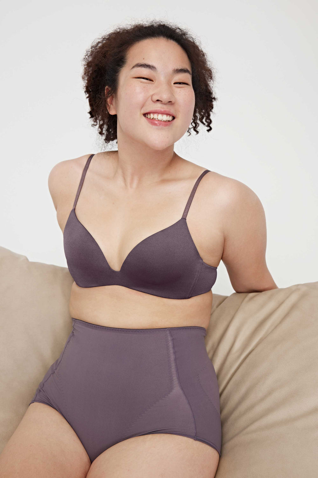 A woman wearing a purple triangle bra and purple panties and sitting on the sofa