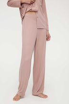A woman wears a pink pajama set and lifts the hem