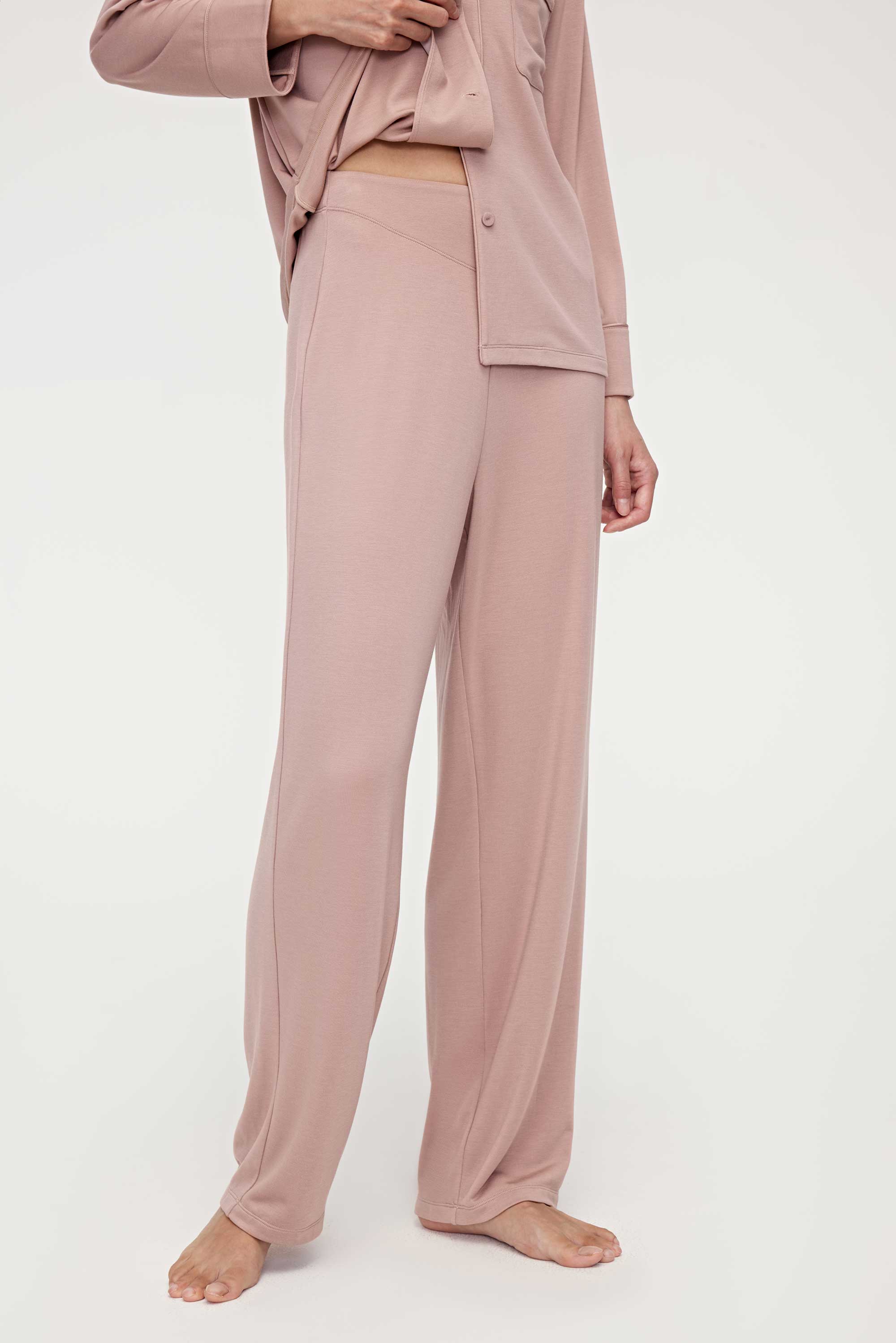 A woman wears a pink pajama set and lifts the hem